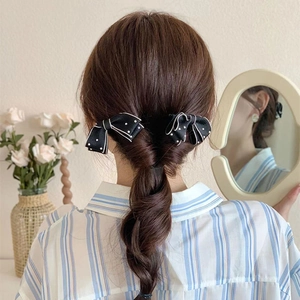 Detail of black polka dot bow hair clips styled on braided hair with pearls
