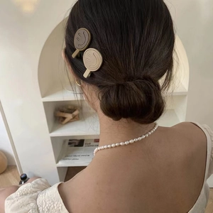 Detail view of smiley face hair clips and pearl necklace styled on model back profile