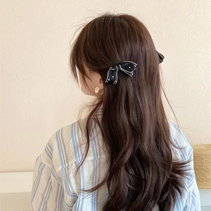 Rear view of model wearing two black and white bow hair clips with pearl accents
