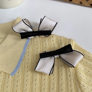 Close-up of white ribbon bow hair clips with black trim on a yellow knit sweater