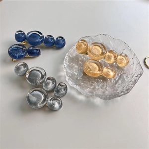 Trois pinces à cheveux bulles en bleu, argent et or sur un plateau en verre