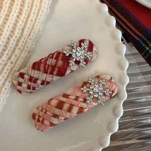 Detail of tweed plaid hair clips featuring crystal snowflake charms on a white ceramic plate