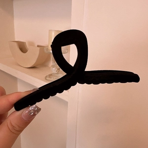 Close-up of minimalist black velvet hair claw clip with cross twisted design in hand