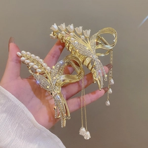 Detailed close-up of golden metal hair claws with lily of the valley and pearl tassels
