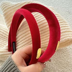 Detail of red velvet headband with golden metal accent on a white knit background