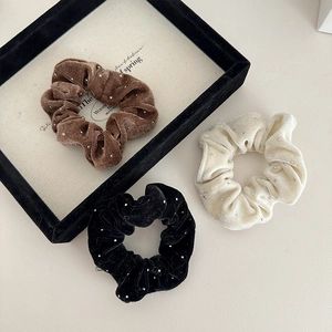 Close-up of velvet scrunchies in black, brown, and beige with sparkling silver beads