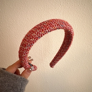 Close-up of a thick red tweed headband with multicolored woven texture and festive style