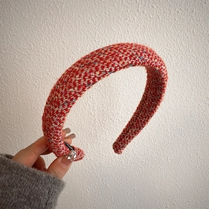 Close-up of a red and white tweed braided headband held by hand for autumn and winter style
