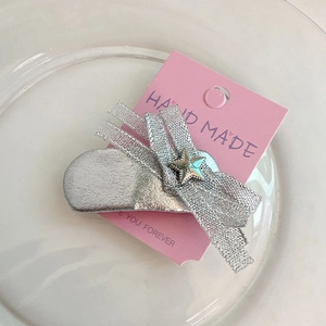 Détail d'une pince à cheveux argentée en forme de nuage avec nœud et étoile sur carton