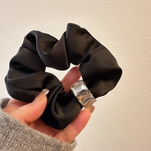 Detailed close-up of a black satin scrunchie featuring a clear rectangular jewel accent
