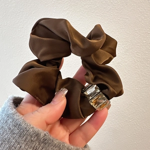 Detailed view of a brown satin hair scrunchie featuring sparkling crystal rhinestones