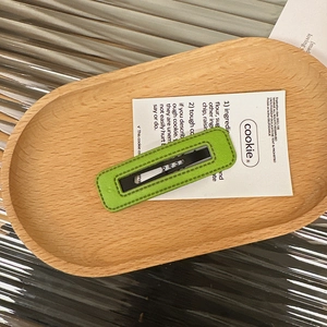 Close-up of a rectangular grass green leather hair clip with lychee texture in a wooden tray