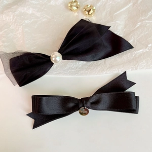 Detail of black satin bow hair clips with pearl accent and metallic logo tag