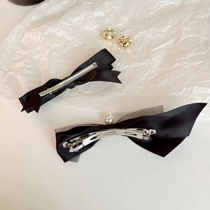 Detailed shot of black bow hair clips with white pearl and satin texture on white surface