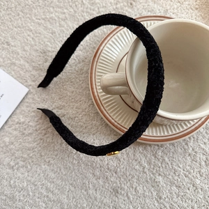 Detail view of black plush fleece headband with gold metal emblem on a soft surface