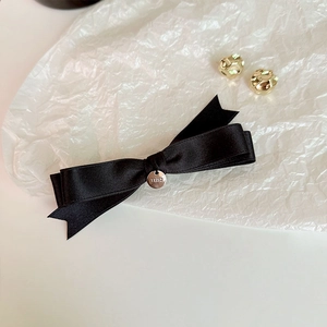 Detail of black silk bow hair clip with silver round logo pendant on white background