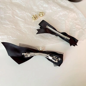 Elegant black satin bow hair clip with pearls and golden sphere earrings set on white paper