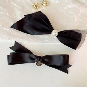 Elegant black bow hair clip set with pearl accent and metal tag on white background