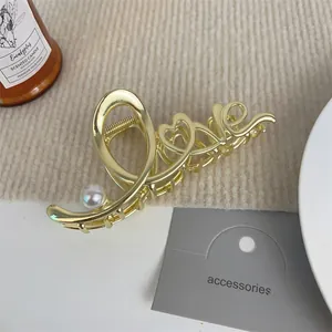 Detail einer goldenen LOVE Haarklammer aus Metall mit Perle auf weichem Strickstoff