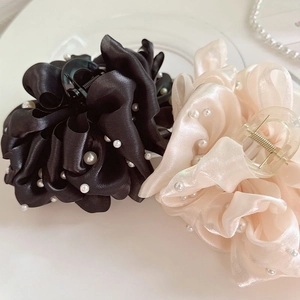 Vue détaillée des pinces à cheveux en satin avec perles noires et beige sur un plateau