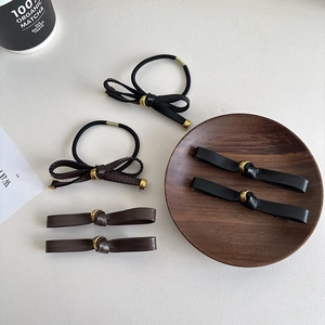 Detail view of minimalist leather bow hair ties and clips in black and brown tones