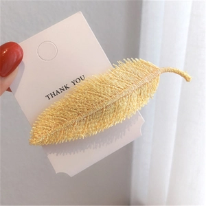 Detail view of a yellow feather-shaped embroidered hair clip on a white card display