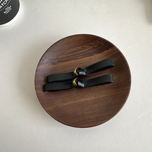 Close-up of minimalist black leather hair clips with gold metal beads on wood tray