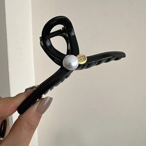 Detail of glossy black hair claw with a large pearl and a golden inspirational tag