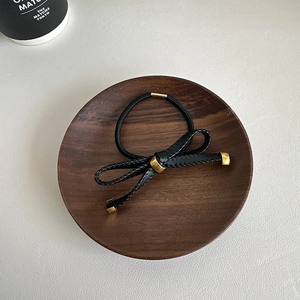 Elegant black woven bow hair tie with gold metal accents on a dark wooden tray