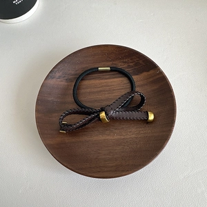Detail of high-elasticity hair tie with brown leather bow and golden metal accents