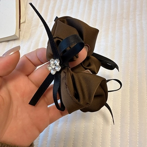 Gros plan sur chouchou en satin marron avec nœud noir et fleur en strass étincelante
