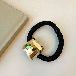 Élastique à cheveux minimaliste avec breloque cube en or poli sur fond neutre