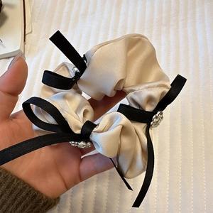 Détail du chouchou en satin beige avec nœud noir et fleur en strass scintillante