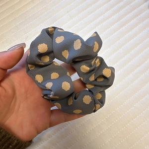 Detailed view of blue satin polka dot scrunchie held in hand to show size and fabric texture