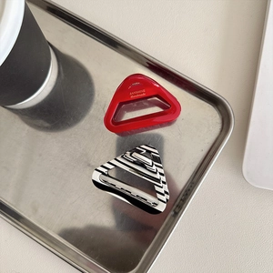 Minimalist triangular acetate hair claws in red and striped patterns on a metal tray