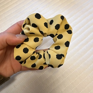 Close-up detail of yellow satin scrunchie with black polka dots and ribbed fabric texture