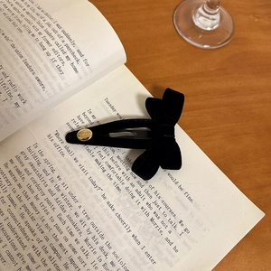 Retro black velvet bow hair clip with gold metal button on vintage book background