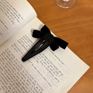 Elegant black velvet bow hair clip with gold bean accent on vintage book page