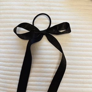 Detail of elegant black silk satin bow hair tie with long ribbons on white fabric