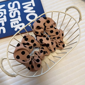 Detailed shot of a beige satin polka dot scrunchie inside a white metal basket