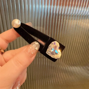 Detail of a black velvet bow hair clip with heart rhinestone and faux pearl decoration