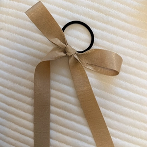 Detail of elegant champagne satin bow hair tie with long ribbons on textured background