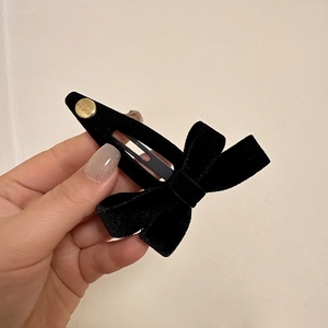Close-up of black velvet bow hair clip with a small gold button and metal snap base