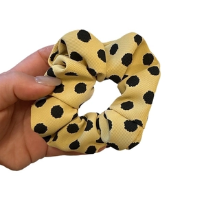 Polka dot satin scrunchie in beige fabric held by hand for a stylish ponytail look