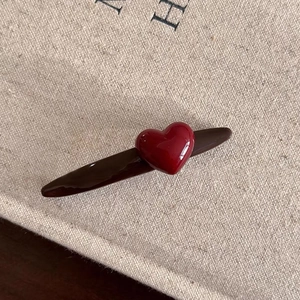 Minimalist red heart duckbill hair clip with glossy base on textured fabric background