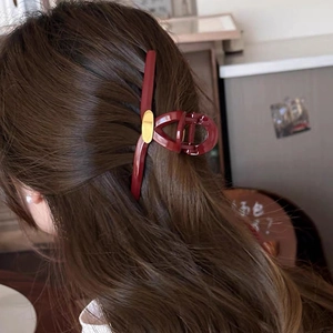 Détail d'une grande pince à cheveux géométrique rouge avec accent doré sur cheveux
