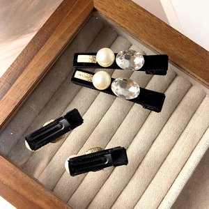 Détail d'une pince à cheveux en velours noir avec perle, cristal et décoration métallique