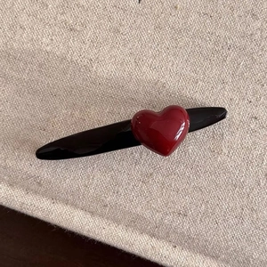 Minimalist red heart hair clip with glossy resin finish on beige fabric background