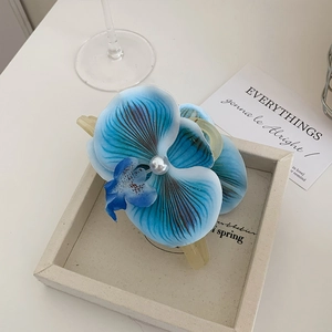 Eleganter Haarclip mit blauer Orchidee, Perle und Farbverlauf auf Holztablett
