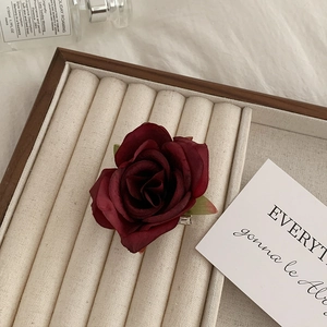 Macro detail of dark red artificial rose shark clip hair accessory on a display tray